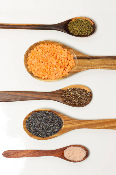 Himalayan pink salt, poppy seeds, chia seeds, pink lentils and oregano on wooden spoons - White background - Photo, Image