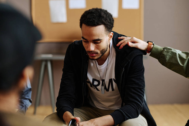 Hand eines jungen Mannes auf der Schulter eines unglücklichen und depressiven männlichen Begleiters einer psychologischen Sitzung oder Selbsthilfegruppe - Foto, Bild