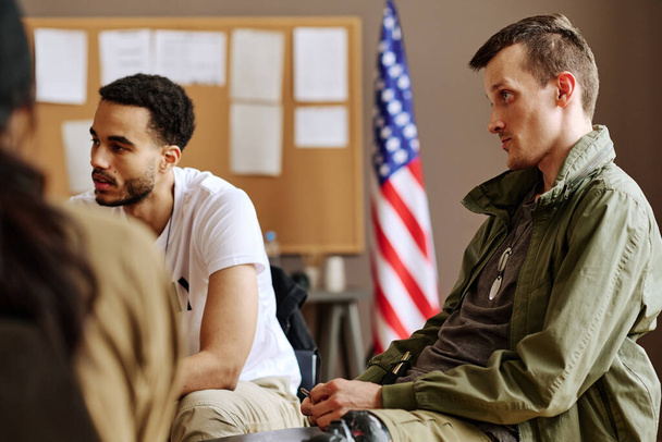 Νεαρός που κοιτάζει ψυχοθεραπευτή και ακούει τις συμβουλές του ενώ κάθεται ανάμεσα στους συνοδούς της ψυχολογικής συνεδρίας - Φωτογραφία, εικόνα