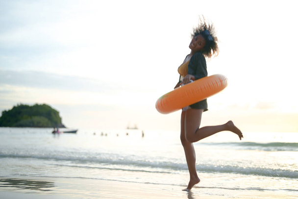 Ritratto sexy asiatico africano signora in piedi e rilassante a spiaggia. L'ora legale al mare e in spiaggia. donna che gioca anello di nuoto giallo sulla spiaggia tropicale. - Foto, immagini