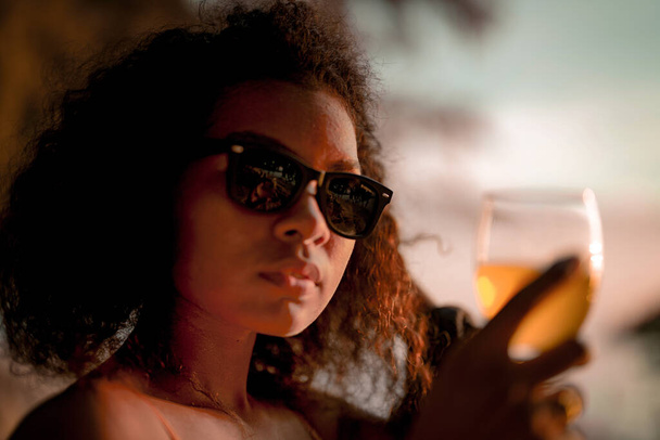 Африканка п "є сік коктейлю, сидячи на лавці пляжу на тропічному пляжі. Молодий мандрівник у жовтому бікіні й витріщається на красу природи. Бажання і подорожі концепт.  - Фото, зображення