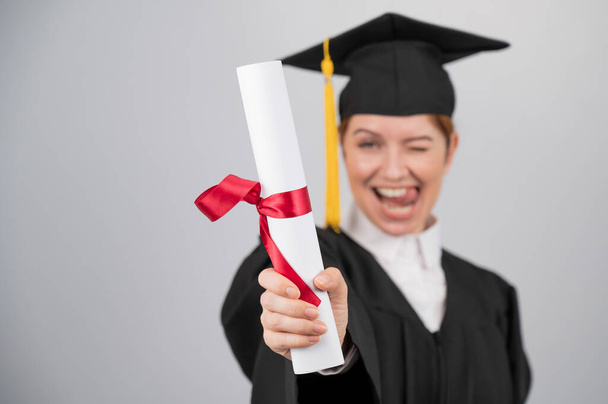 Emotional woman in graduate gown holding diploma in foreground - Foto, Imagem