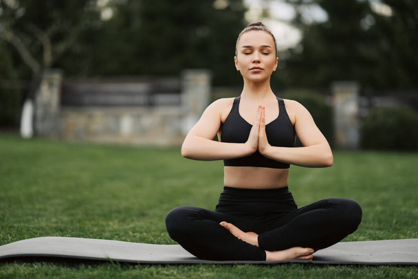 Yoga im Freien. Glückliche Frau macht Yoga-Übungen, meditiert im Park. Yoga-Meditation in der Natur. Konzept der gesunden Lebensweise und Entspannung. Hübsche Frau praktiziert Yoga im Gras. - Foto, Bild