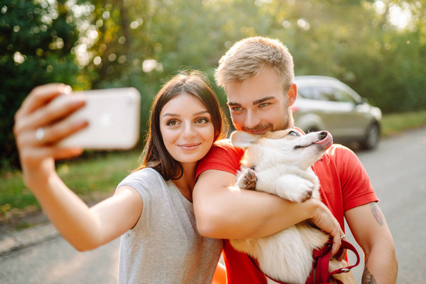 Selfie time. Young couple together with their beloved pet on a walk doing selfie.The concept of an active lifestyle, travel, love and vacation. Pet and human. - 写真・画像