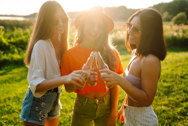 Three woman resting in nature in the picnic drinking beer, cheers. Vacation, picnic, friendship or holliday concept. - Foto, imagen