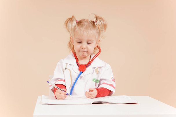 A child dressed as a doctor takes notes in a notebook and listens attentively to the patient. High quality photo - Foto, immagini