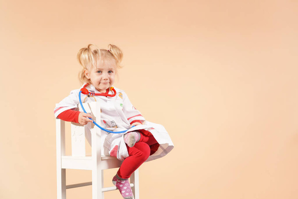 A child with a stethoscope on a white chair plays doctor. Little girl doctor. - Foto, Imagem