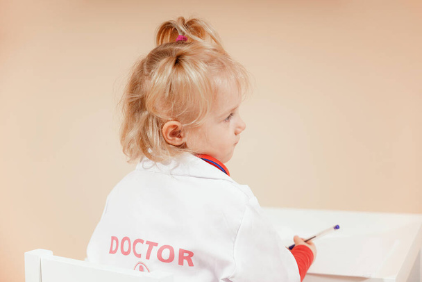 A child dressed as a doctor takes notes in a notebook and listens attentively to the patient. High quality photo - Foto, imagen