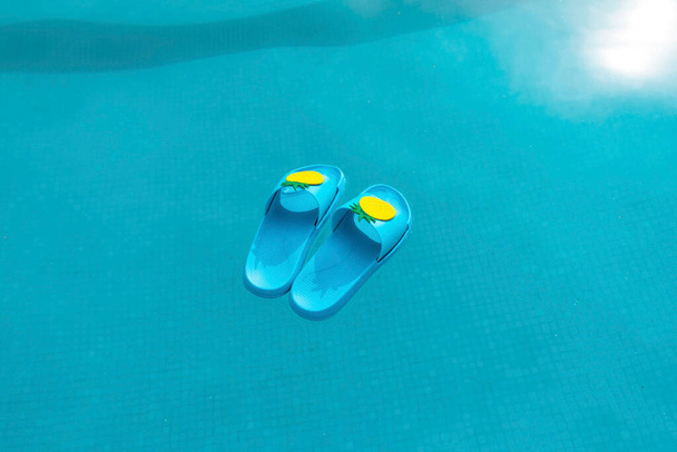 Blaue Poolsandalen schwimmen im Wasser eines Swimmingpools. Sommerkonzept. - Foto, Bild