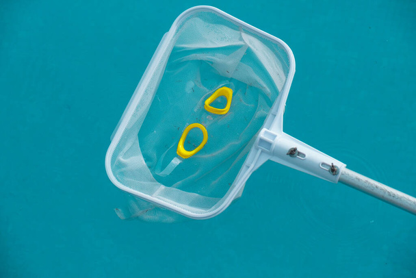 Un filet de nettoyage de piscine recueille les verres de piscine jaunes de l'eau. Concept d'été. Esthétique été. - Photo, image