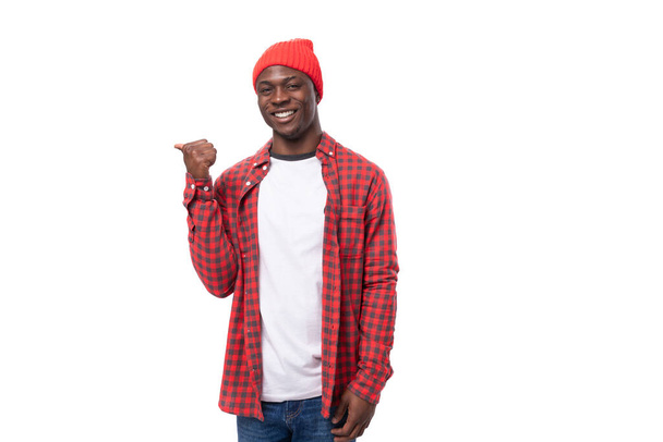 selbstbewusster junger ethnisch-afrikanischer Typ im stylischen Look, der mit dem Zeigefinger auf ein Werbeangebot auf weißem Hintergrund zeigt. - Foto, Bild