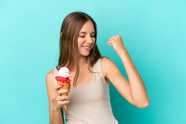 Young Lithuanian woman with cornet ice cream isolated on blue background celebrating a victory - Fotó, kép