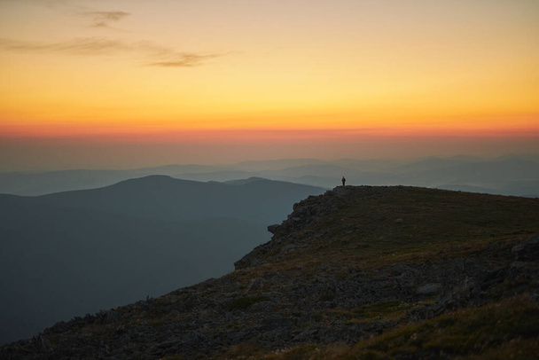 Man looking at sunrise. Mountains at sunrise. Man standing on peak. Natural mountain landscape with illuminated misty peaks, foggy slopes and valleys, blue sky with orange yellow sunlight. Amazing scene from Beskid Zywiecki in Poland - Foto, imagen