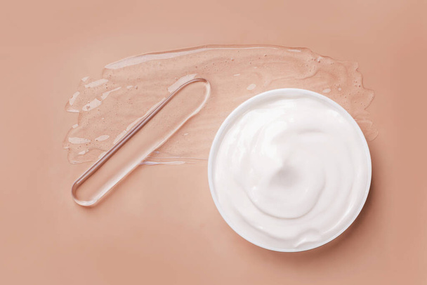 Smeared transparent gel on the background. Spatula for applying cream. A round jar of cosmetic white cream. On a beige background. - Photo, Image