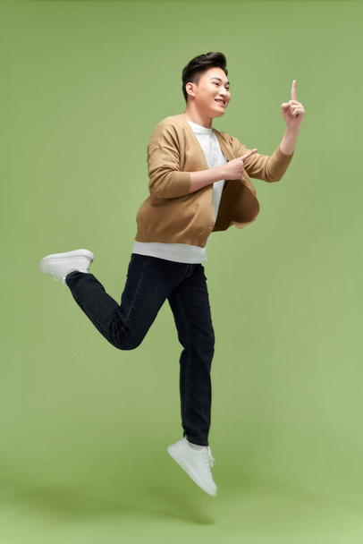 Энергичный возбужденный молодой азиат прыгает и указывает рукой на пустое пространство в сторону  - Фото, изображение