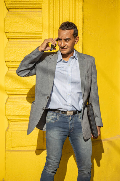 Young latino man talking on the mobile phone isolated on yellow background. - Valokuva, kuva