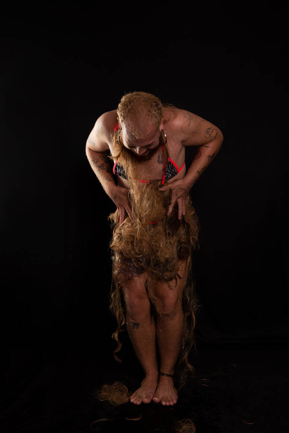 Young man, wearing bikini, gluing hair on body. Expression of pain. Performance female gorilla. isolated on dark background. - Fotó, kép