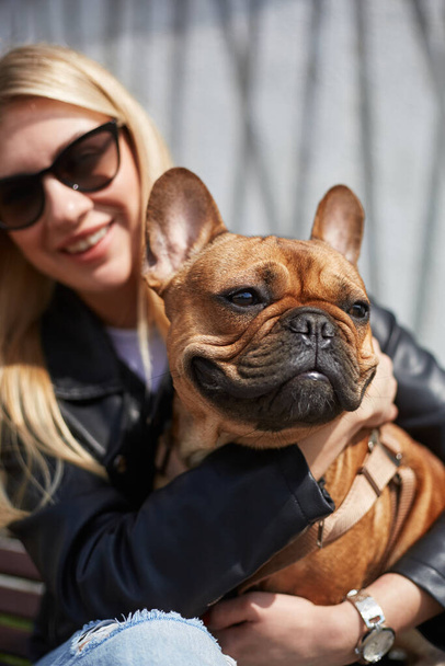 Portrait of a cute French bulldog sitting on the owner's laps. Happy pet owner woman embracing her young brown doggy with a smile - Fotoğraf, Görsel