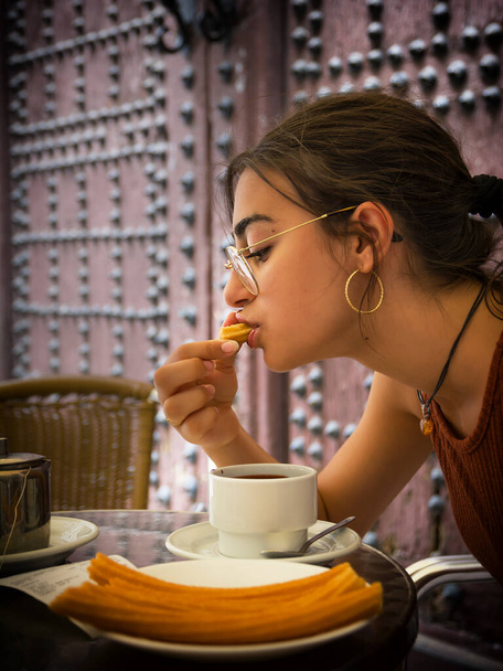 Young girl savors a snack of churros and a cup of hot chocolate - 写真・画像