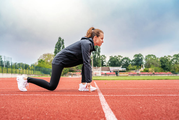 Mladá žena běžec v počáteční pozici na běžecké trati při práci ven. - Fotografie, Obrázek