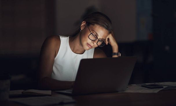 Als stress je beste kant overschaduwt. een jonge zakenvrouw op zoek versleten tijdens het gebruik van een laptop tijdens een late nacht op het werk - Foto, afbeelding