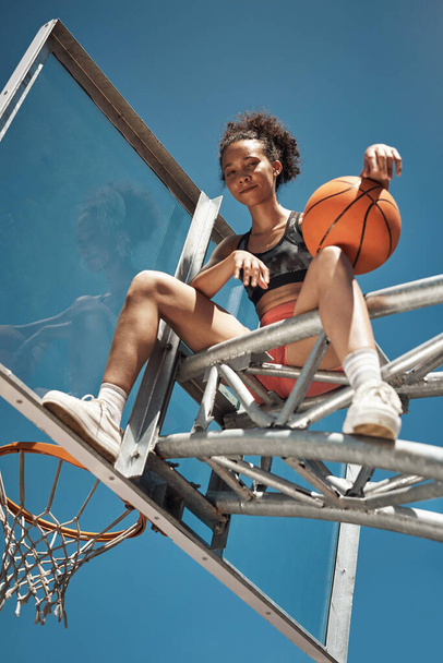 Keep calm and shoot hoop. Portrait of a sporty young woman sitting on a basketball hoop on a sports court - Foto, Imagem