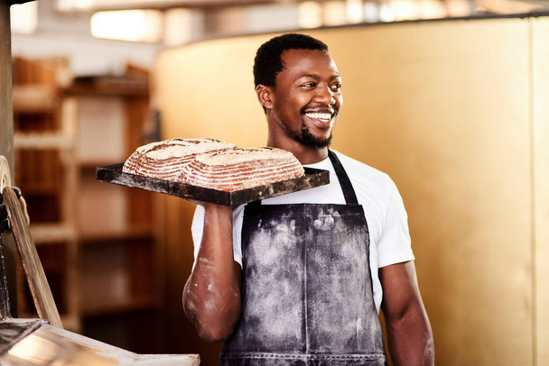 Als het je vreugde brengt, blijf het dan doen. een mannelijke bakker houdt vers gebakken brood in zijn bakkerij - Foto, afbeelding