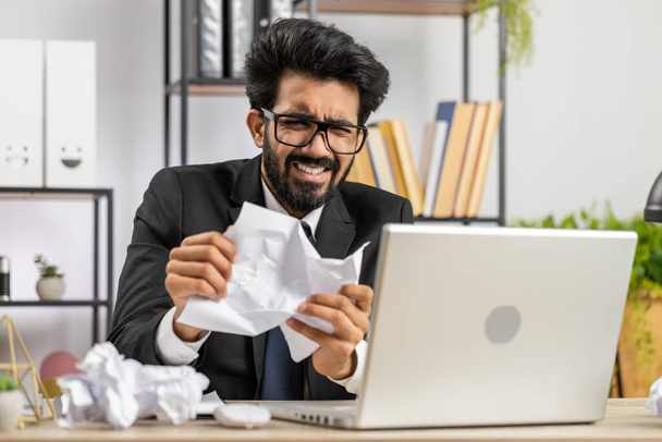 Dühös, dühös indiai férfi dolgozik az irodában dobott gyűrött papír, amelynek idegösszeroppanás a munkahelyen, migaine, fejfájás, stresszkezelés, mentális szorongás problémák, elvesztése temperamentum, reakció a kudarc - Fotó, kép