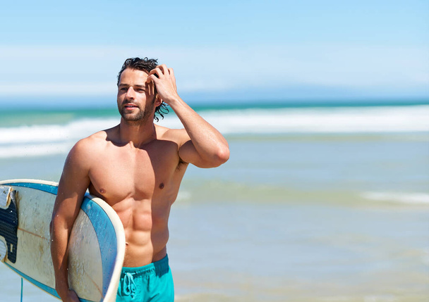 Surfen hält ihn in guter Form. Ein attraktiver junger Mann geht mit seinem Surfbrett aufs Wasser - Foto, Bild