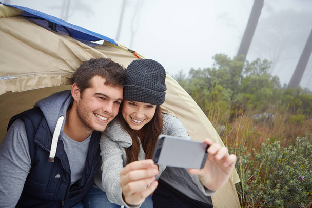 Having the time of their lives in nature. a young couple taking a photo of themselves while sitting inside a tent - Фото, изображение