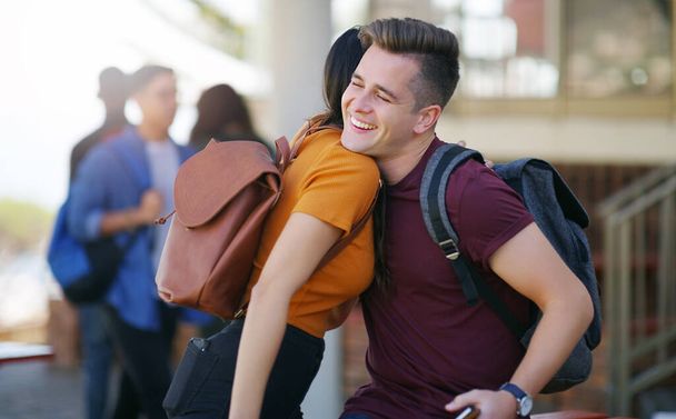 Qué bueno verte de nuevo. dos jóvenes estudiantes alegres saludándose con un abrazo mientras esperan para ir a clase fuera de una escuela - Foto, imagen