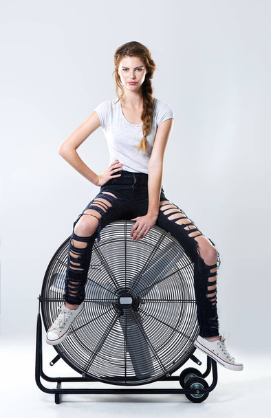 Se on hieno itseluottamus. Studio muotokuva houkutteleva nuori nainen istuu päälle suuri sähköinen tuuletin - Valokuva, kuva