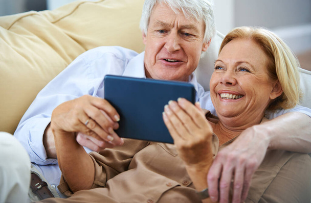 That clip was hilarious. a happy elderly couple watching something on a digital tablet while relaxing on their sofa - Fotó, kép
