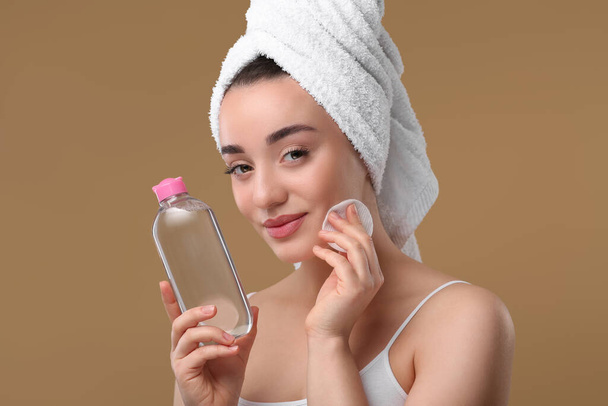 Beautiful woman in terry towel removing makeup with cotton pad on beige background - Foto, Bild