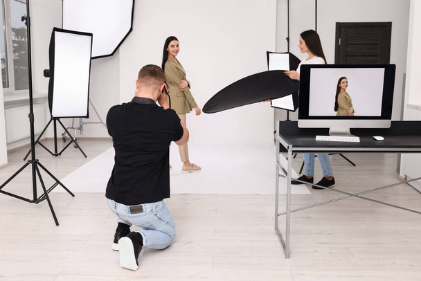 Professional photographer and assistant working with beautiful model in modern photo studio - Photo, image