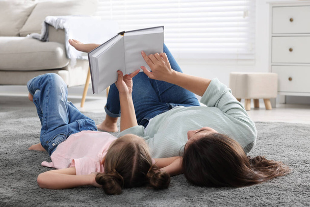Young mother and her daughter reading book on floor at home - Foto, afbeelding