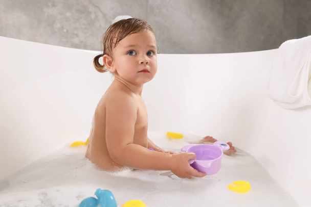 Cute little girl taking bubble bath with toys indoors - Foto, afbeelding
