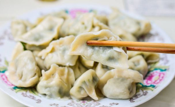 Chopsticks picks up the boiled Chinese dumplings (Jiaozi) from a plate.  - Foto, afbeelding