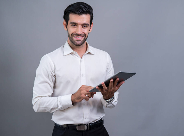 Confident businessman in formal suit holding tablet with surprise look for promotion or advertising. Facial expression and gestures indicate excitement and amazement on an isolated background. Fervent - Foto, Imagem