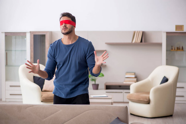 Blindfolded young man seeking at home - 写真・画像