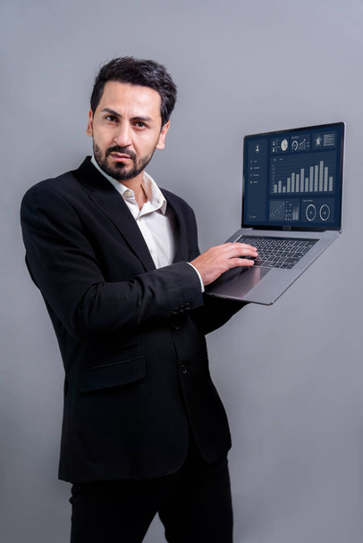 Successful businessman in black suit with innovative tech concept, standing pose and holding laptop and smiling with excitement on copyspace background for promotion or advertisement. Fervent - Fotó, kép