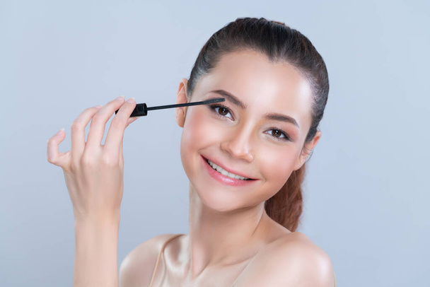 Closeup woman with blond hair putting glamorous black mascara with brush in hand on long thick eyelash. Perfect soft natural cosmetic makeup clean facial skin young woman in isolated background. - Foto, immagini