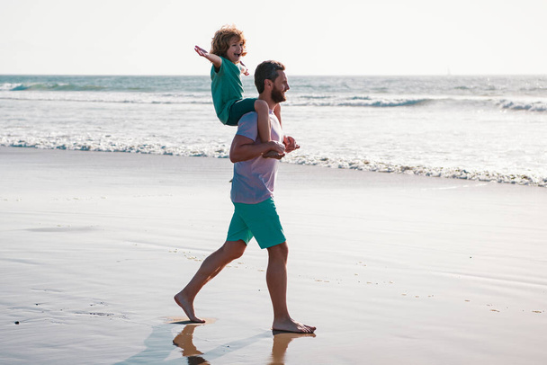 Father and son walking on sea. Handsome man father carrying young boy son. Happy dad holding child. Daddy with kid boy on a summer day. Concept of friendly family and of summer vacation - Φωτογραφία, εικόνα