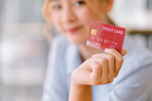 オンライン電子商取引、キャッシュバック、ローン、支払い、債務ショッピングのためのモックアップ赤いクレジットカードを示すアジアの若い女性銀行クライアントの顧客のクロップショット - 写真・画像