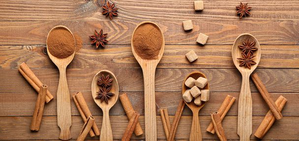 Spoons with cinnamon, anise and sugar on wooden background, top view - Photo, Image