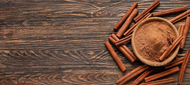Bowl of natural cinnamon powder and sticks on wooden background with space for text, top view - Photo, Image