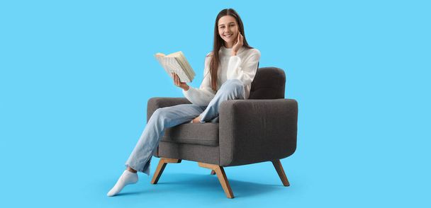 Mulher bonita leitura livro em poltrona no fundo azul - Foto, Imagem