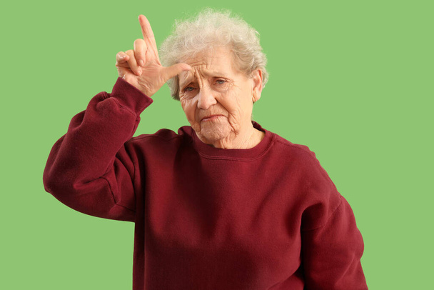Vanhempi nainen osoittaa häviäjä ele vihreällä taustalla - Valokuva, kuva
