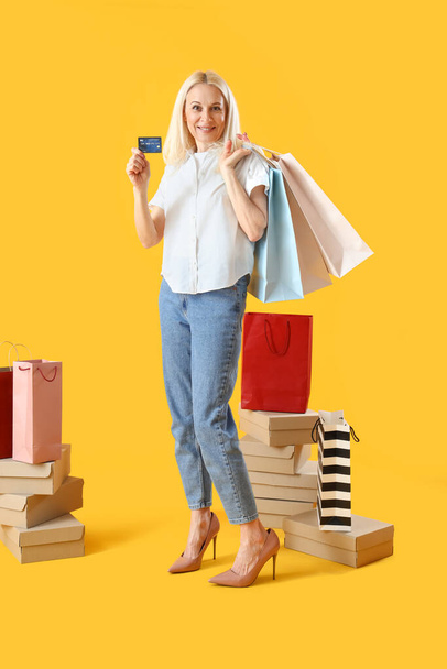Mature woman with shopping bags and credit card on yellow background - Fotoğraf, Görsel