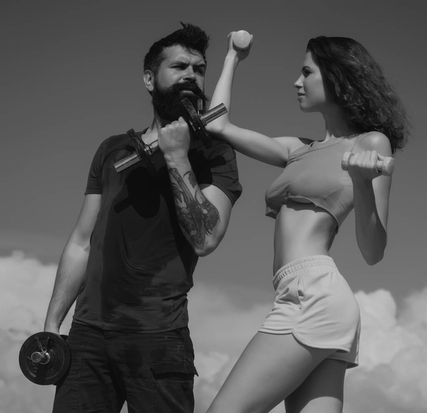 Fit sexy couple on sky background with dumbbells. Fitness concept. Sports couple training with dumbbell. Healthy coupl life style. Fitness sexy models pumping up arm with dumbbell - Фото, зображення
